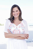 A long-haired woman wearing a white summer dress with colourful embroidery detail