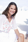 A long-haired woman wearing a white summer dress with colourful embroidery detail