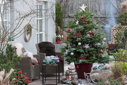 Weihnachtsterrasse mit geschmückter Nordmanntanne als Weihnachtsbaum, Korbsessel und Feuerschale