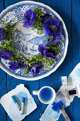 Wreath of anemones on blue plate, artists' pastels and painting utensils