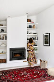 Woman standing in front of shelves next to fireplace in living room