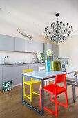 Schlichte graue Küchenzeile davor Esstisch mit verschiedenfarbigen Designerstühlen