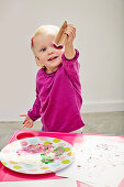 Kleines Mädchen stempelt mit Papprolle bunte Farbherzen auf Papier