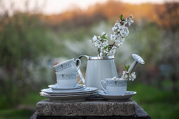 White coffee service and apple blossom in watering can on stone slab outside