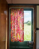 Red, floral curtain on door of old caravan
