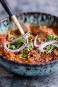 A bowl of beef curry with red onions and coriander