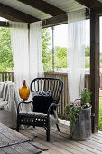 Black rattan chair on roofed terrace with curtains