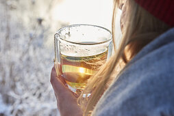 A woman wearing winter clothing drinking a cup of tea outside