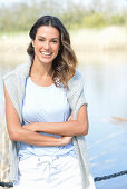 Junge Frau in hellblauem T-Shirt, Pulli über den Schultern und weißen Shorts am Fluss