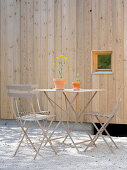 Metal garden table and chairs next to external wall of house made from pale wood