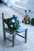 Christmas wreath on child's chair with teddy bear in background