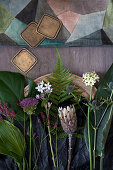 Still-life arrangement of flowers and leaves (hosta leaves, Swiss cheese plant leaf, sea lavender, allium, milkweed, fern, protea, Star-of-Bethlehem, sea holly, bird of paradise leaf)