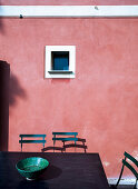 Tisch mit Stühlen vor rosa Fassade mit kleinem Fenster