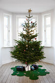 Decorated Christmas tree on rug made from green circles in room with bay window