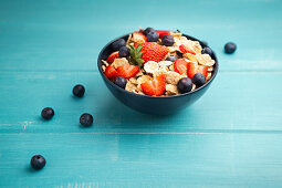 Breakfast bowl of corn flakes with strawberries and blueberries on wooden blue background