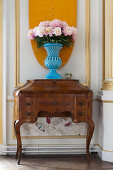 Pfingstrosen in blauer Vase auf altem Sekretär vor Kassettenwand