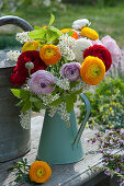 Colorful bouquet of ranunculus and bird cherry in a turquoise tin can