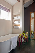 Free-standing bathtub in bathroom with shelves in niches and flower arrangement with amaranth