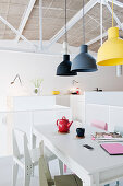 Industrial lamps above dining table and colourful chairs in loft apartment