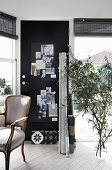 Baroque chair, black pinboard on door and olive branches in floor vase in study