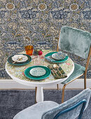 Set table with floral top next to wall with vintage-style floral wallpaper