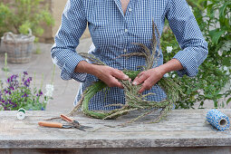 Tying a giant pretzel from grass Woman bends a bundle of grass stiffened and wrapped with wire into a pretzel shape