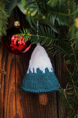 Knitted decoration in shape of Christmas tree hung from conifer branch