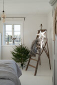 Small Christmas tree next to old stepladder decorated with fur blanket and paper star