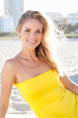 A blonde woman on a beach wearing a yellow bandeau dress