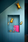 Golden decorative bugs on blue wall with niche and pink present