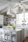 Pendant lamps above island counter with bar stools in white, country-house kitchen