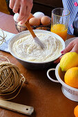 From above anonymous woman using wooden spatula to mix pastry batter near eggs and citrus juice on kitchen table