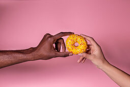 Crop anonymous multiethnic couple holding delicious fresh doughnut on pink background