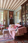 Sofa mit rosa Überwurf vor hohem, antikem Bücherregal mit Glasfront