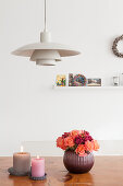 Klassikerlampe über Esstisch mit Blumenstrauß und Kerzen