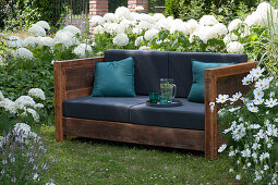 Sofa in the garden to live outside in summer, surrounded by shrub hydrangeas and garden cosmos