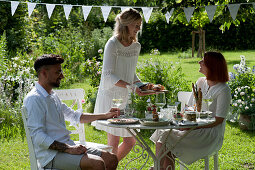 Friends at the set table in the garden, woman hands bread