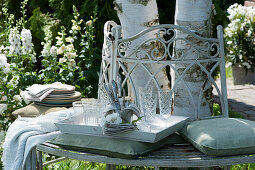 White tray with glasses and cutlery on tree bench, branch with rose petals