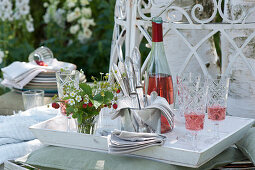 Weißes Tablett mit Strauß aus Walderdbeeren, Besteck und Servietten, Rosato in Flasche und Gläsern