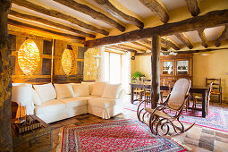 Sofa set and rocking chair in open-plan interior with rustic wood-beamed ceiling