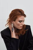 A red-haired woman wearing earrings and a black blazer
