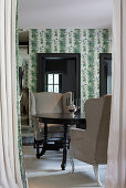 Round, antique wooden table and armchairs in room with botanical wallpaper