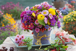 Autumn bouquet made of asters, chrysanthemums, summer asters, rose hips and apples, vase covered with felt