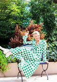 A grey-haired woman sitting on a park bench wearing a polka-dot maxi dress