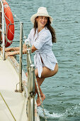 Brünette Frau mit Hut in gestreifter Hemdbluse und Bikini am Boot