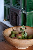 Birnen in einer Holzschale auf der Ofenbank am grünen Kachelofen