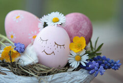 Pot as a decorative Easter basket with an Easter egg with a drawn face, daisies, buttercups, grape hyacinth, and feather