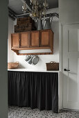 Suitcases and zinc jugs on a wooden wall cupboard with storage space behind a curtain