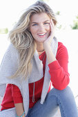 A young blonde woman wearing a red jumper with a light-coloured jumper over her shoulders