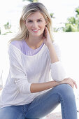 A young blonde woman wearing a purple t-shirt and a white jumper
